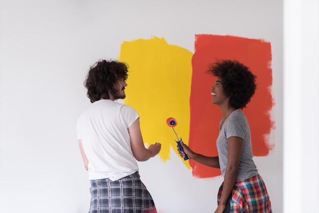 szczęśliwa młoda wieloetniczna para malująca wewnętrzną ścianę nowego domu