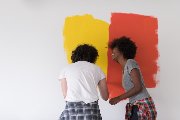 szczęśliwa młoda wieloetniczna para malująca wewnętrzną ścianę nowego domu
