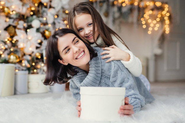 Szczęśliwa modelka z krótkimi ciemnymi włosami i jej urocza mała dziewczynka bawią się razem świętują świąteczną wymianę prezenty mają uśmiechnięte miny mają radość Przyjazna rodzina z prezentami