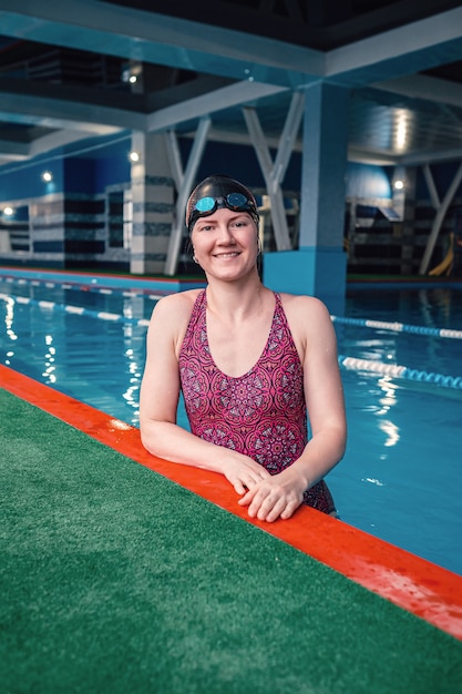 Szczęśliwa muskularna pływaczka w okularach i czapce na basenie i reprezentuje koncepcję zdrowia i dopasowania, ideę sportu, zdrowego stylu życia i wypoczynku