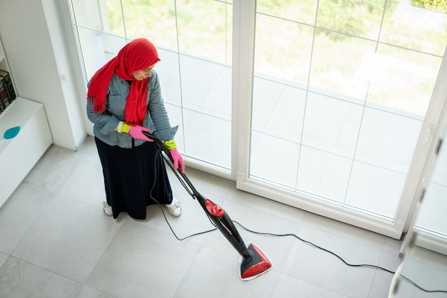 Szczęśliwa muzułmańska kobieta czyści nowoczesny dom żywy pokój. Wysokiej jakości zdjęcie