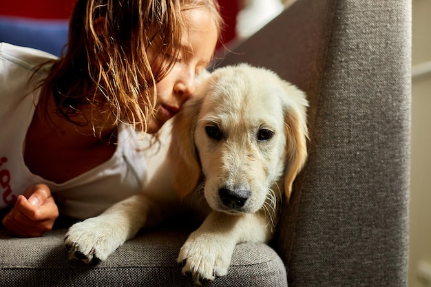 Szczęśliwa nastolatka leżąca na kanapie i obejmująca swojego szczeniaka golden retrievera