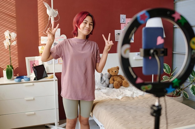 Zdjęcie szczęśliwa nastolatka pokazująca gesty pokoju publiczności internetowej