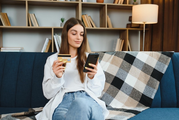 Szczęśliwa nastolatka robi zakupy online siedząc na kanapie w domu Młoda kobieta wstawia numer karty kredytowej na stronie internetowej za pomocą swojego smartfona