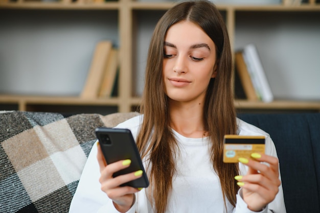 Szczęśliwa nastolatka robi zakupy online siedząc na kanapie w domu Młoda kobieta wstawia numer karty kredytowej na stronie internetowej za pomocą swojego smartfona