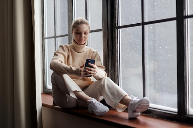Szczęśliwa nastolatka sprawdzająca media społecznościowe, trzymająca smartfon w domu, korzystająca z telefonu komórkowego podczas zakupów online