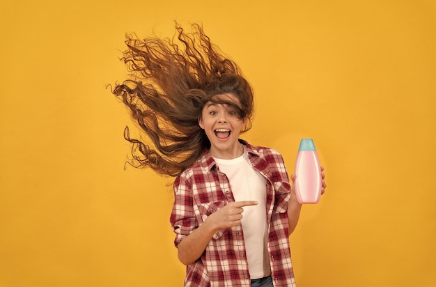 Szczęśliwa nastolatka z długimi kręconymi włosami trzyma butelkę szamponu piękna