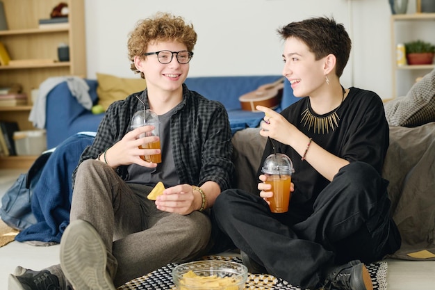 Szczęśliwa nastolatka z szklanką soku lub napoju gazowanego patrząca na swojego chłopaka