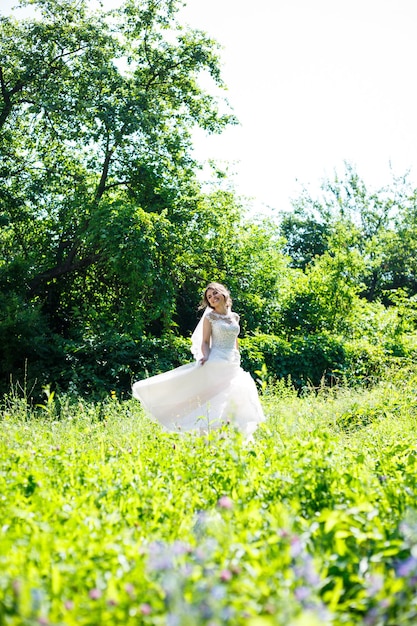 Szczęśliwa panna młoda dziewczyna w długiej białej sukni ślubnej i wirować welon w zielonym parku na przyrodę.