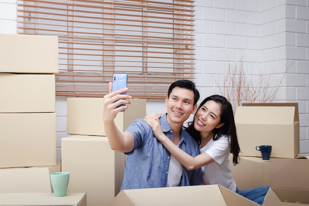 Szczęśliwa Para Azjatyckich Wprowadza Się Do Nowego Domu Weź Smartfon I Zrób Selfie. Koncepcja Rozpoczęcia Nowego życia Zbuduj Rodzinę. Skopiuj Miejsce
