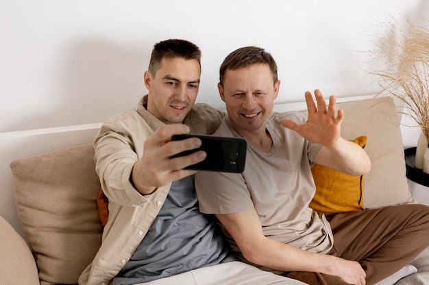 Szczęśliwa para gejów w zwykłych ubraniach, trzymająca smartfona i rozmawiająca z przyjaciółmi online podczas wideorozmowy Związki homoseksualne i alternatywna miłość