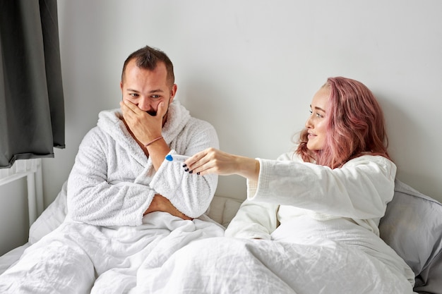 Szczęśliwa para kaukaski jest podekscytowana pozytywnym testem ciążowym na łóżku rano, szczęśliwa reakcja, mężczyzna jest zaskoczony
