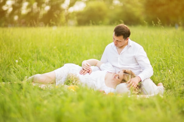 Szczęśliwa para - kobieta w ciąży i jej mąż siedzą na trawie w parku.