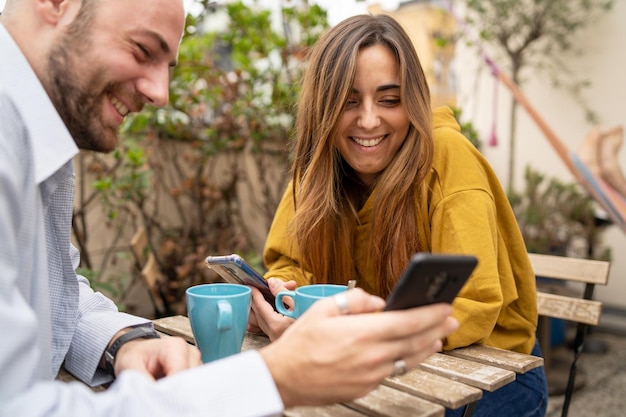 Szczęśliwa Para Korzystających Z Treści Multimedialnych W Inteligentny Telefon, Siedząc Na Stoliku Kawiarnianym, Pijąc Kawę.