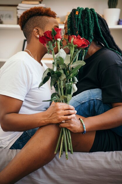 Szczęśliwa para lesbijek trzymająca róże i całująca się w sypialni