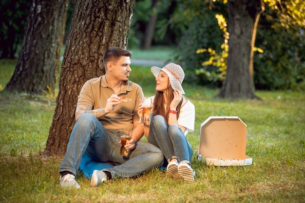 Szczęśliwa Para Na Pikniku W Parku. Jeść Pizzę I Pić Piwo