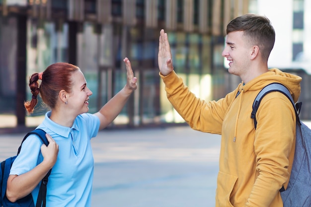 Szczęśliwa Para Pozytywnych, Dwóch Studentów Uniwersytetu, Którzy Odnieśli Sukces, Dając Piątkę, Stojąc Z Plecakami, Uśmiechając Się.