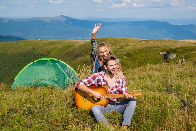 Szczęśliwa para przyjaciół biwakujących i grających razem na gitarze latem w lesie przyrody zakochana para...