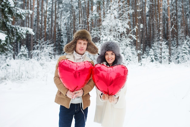 Szczęśliwa para przytulanie i całowanie na świeżym powietrzu w zimowym lesie. Balony w kształcie serca