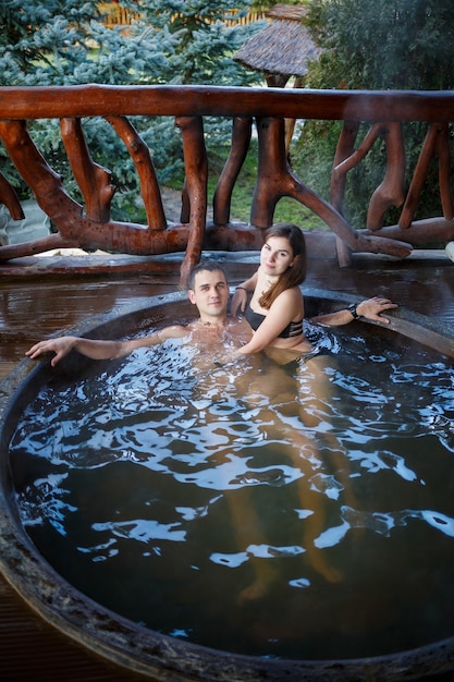 Szczęśliwa para romantycznych kąpieli w jacuzzi, na świeżym powietrzu na romantycznych wakacjach na rozmytym tle przyrody w letnim kurorcie. Jacuzzi na świeżym powietrzu.