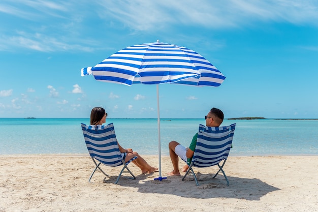 Szczęśliwa Para Siedzi Na Krzesłach Pod Parasolem Na Tropikalnej Plaży. Koncepcja Wakacji Letnich.