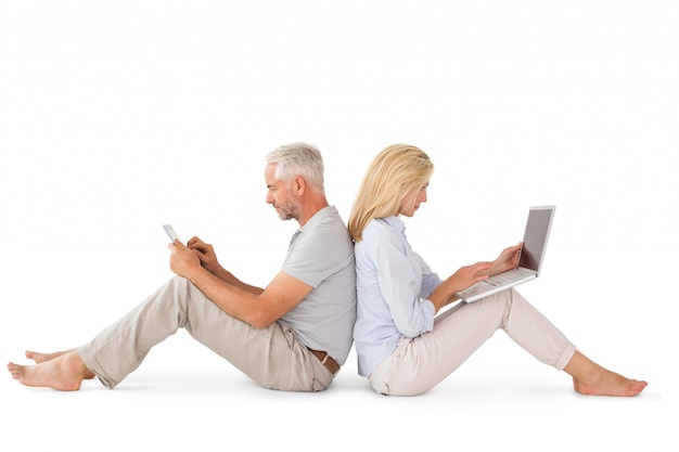Szczęśliwa para siedzi przy użyciu komputera przenośnego i tabletu