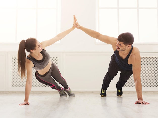 Szczęśliwa para sportowy dając sobie piątkę podczas robienia razem push up w siłowni. Jedność i wsparcie, kopia przestrzeń