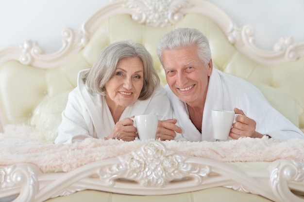 Szczęśliwa para starszych czytająca w łóżku z herbatą