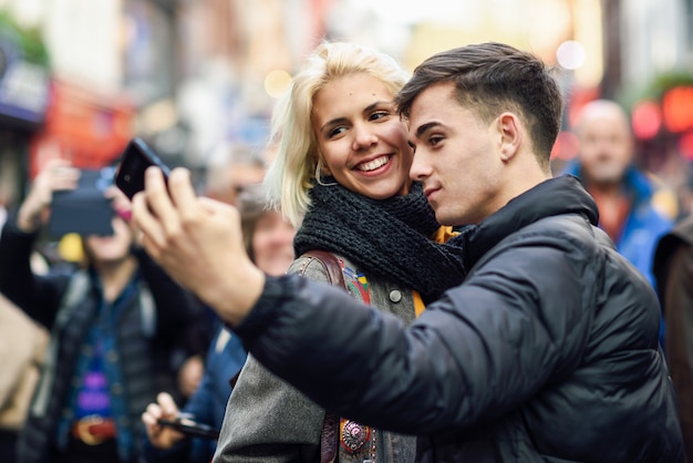 Zdjęcie szczęśliwa para turystów biorąc selfie w zatłoczonej ulicy.