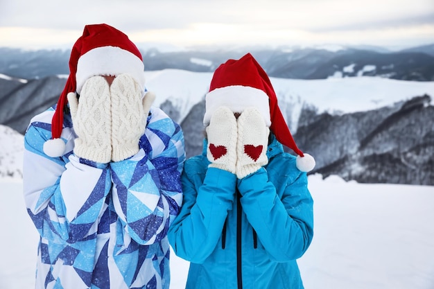 Zdjęcie szczęśliwa para w czapkach mikołaja i ciepłych rękawiczkach bawi się w zaśnieżonym kurorcie. ferie zimowe