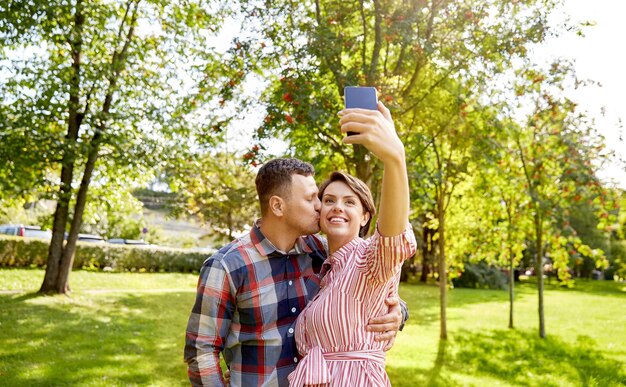szczęśliwa para w parku robiąca selfie za pomocą smartfonu