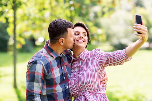 szczęśliwa para w parku robiąca selfie za pomocą smartfonu