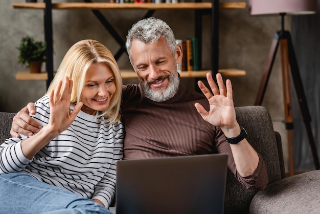 Szczęśliwa para w średnim wieku nawiązująca wideorozmowę za pomocą laptopa