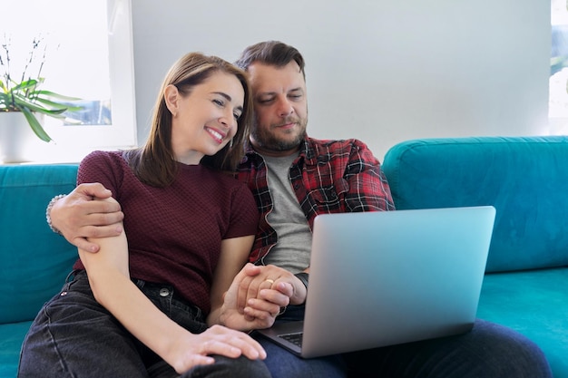Szczęśliwa para w średnim wieku siedzi na kanapie z laptopem