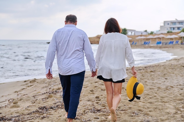 Szczęśliwa para w średnim wieku spacerująca razem na plaży widok z tyłu