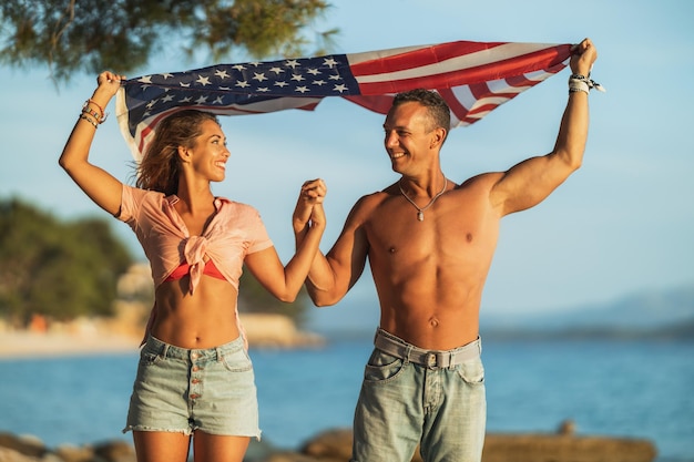Szczęśliwa para z amerykańską flagą narodową spędzającą relaksujący dzień na plaży.