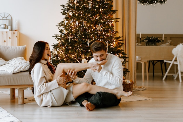 szczęśliwa para zakochana w białym przytulnym salonie z dekoracjami świątecznymi i choinką