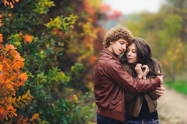 Szczęśliwa para zakochanych jesienią. kędzierzawy wąsaty mężczyzna i rudowłosa kobieta w skórzanych kurtkach i dżinsach czule obejmują