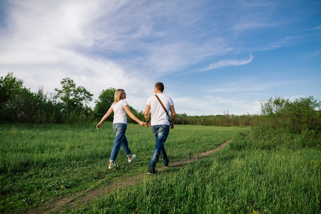 szczęśliwa para zakochanych, trzymając się za ręce na spacerze w zielonym polu