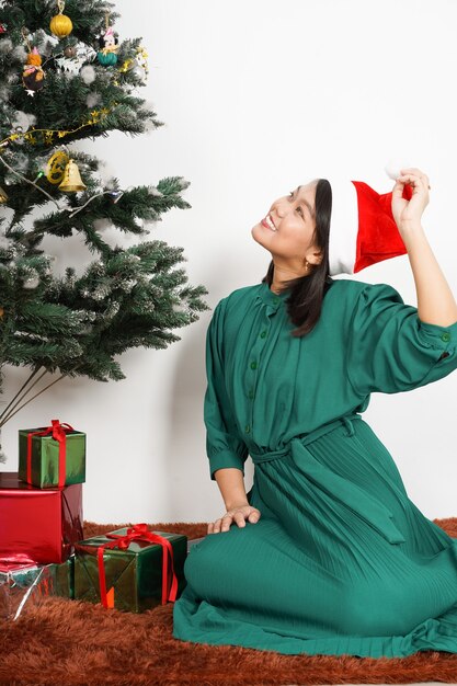 Szczęśliwa piękna Azjatycka kobieta ubrana w zieloną sukienkę i kapelusz Świętego Mikołaja Świętowanie bożonarodzeniowe trzymająca prezent