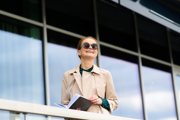 Szczęśliwa piękna bizneswoman z okularami przeciwsłonecznymi, telefonem, laptopem, filiżanką kawy na ulicach miasta