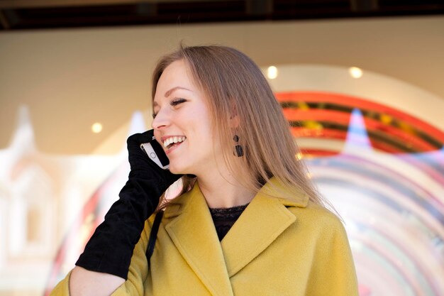 Zdjęcie szczęśliwa piękna dziewczyna dzwoni przez telefon w żółtym płaszczu