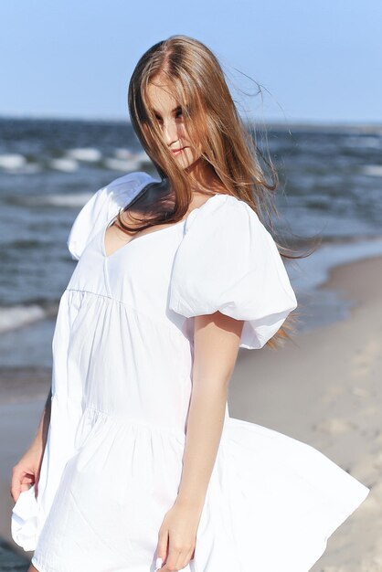 Szczęśliwa, piękna kobieta na plaży oceanu stojąca w białej letniej sukience. Portret