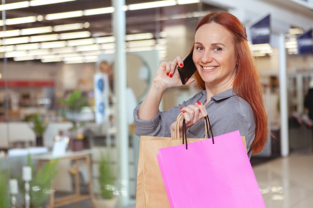 Szczęśliwa piękna kobieta opowiada na telefonie podczas gdy robiący zakupy przy centrum handlowym, kopii przestrzeń. Konsumpcjonizm, koncepcja sprzedaży
