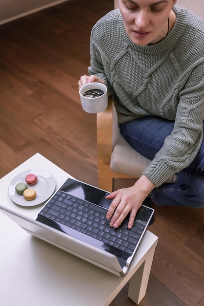 Szczęśliwa piękna kobieta pracuje na laptopie siedząc na fotelu w domu