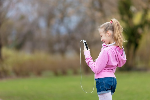 Szczęśliwa piękna mała dziewczynka słuchania muzyki z inteligentnego telefonu w parku.