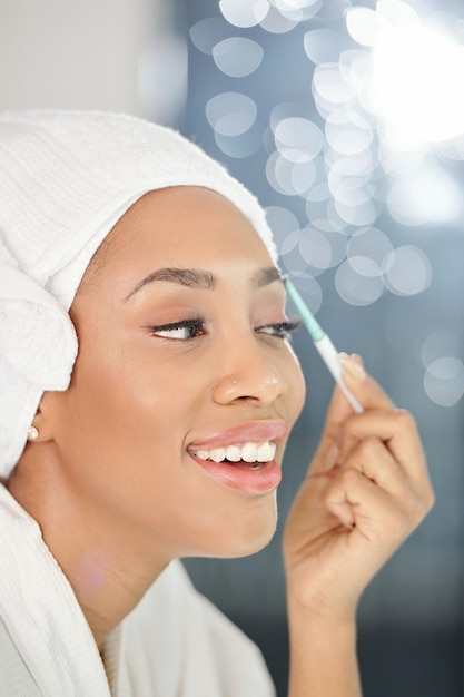 Szczęśliwa piękna młoda czarna kobieta przycinanie brwi z elektrycznym trymerem przed lustrem po wzięciu prysznica rano