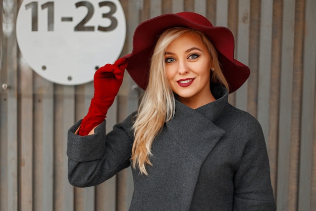 Szczęśliwa piękna młoda kobieta w stylowy kapelusz modny szary płaszcz w pobliżu drewnianej ściany