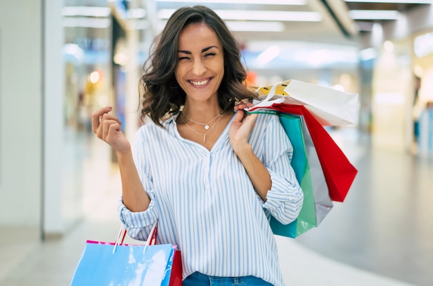 Szczęśliwa piękna młoda stylowa kobieta z torby na zakupy spaceru w centrum handlowym
