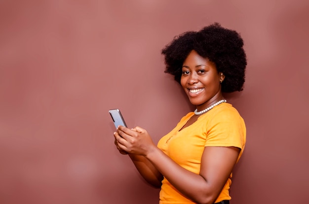 Szczęśliwa podekscytowana afroamerykańska dama na fryzurę Afro za pomocą telefonu komórkowego w studio stojącym za pustym tłem